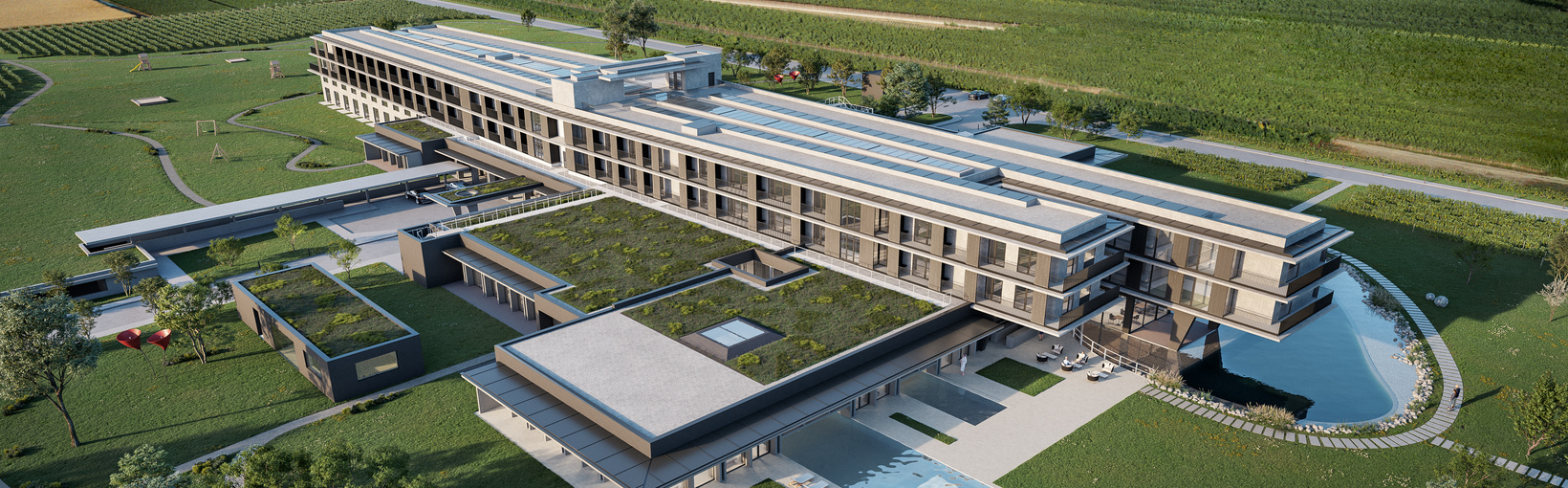 Ein moderner, großer Gebäudekomplex, umgeben von grünen Feldern und begrünten Wegen unter blauem Himmel.