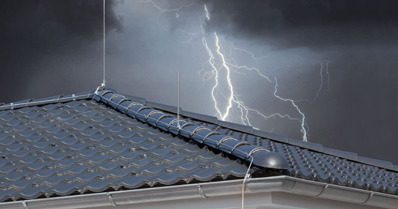 Ein Blitz schlägt in den Himmel über einem Haus mit einem metallenen Blitzableiter auf seinem Ziegeldach ein.