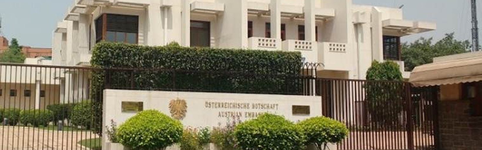 Weißes, modernes Gebäude mit grünem Vorgarten und einem Schild mit der Aufschrift Australian High Commission.