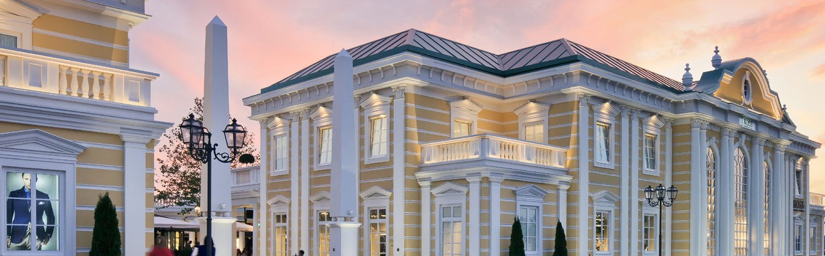 Elegantes gelbes neoklassizistisches Gebäude mit Säulen bei Sonnenuntergang, unter einem farbenfrohen Himmel.