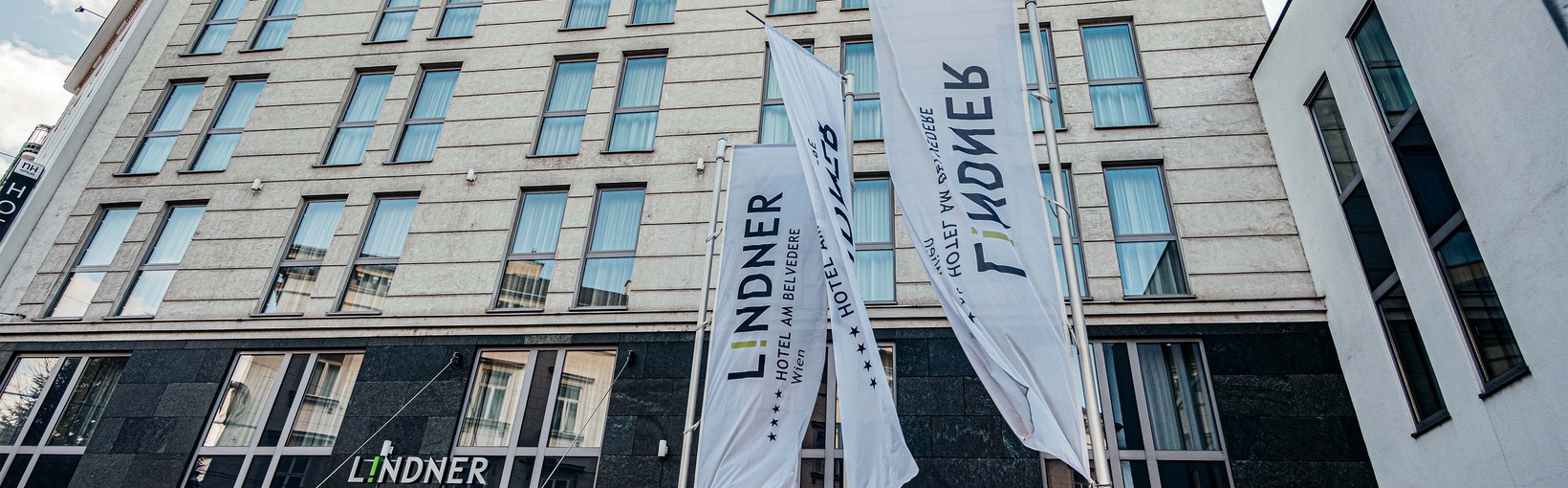 Modernes Hotelgebäude mit großen Fenstern und drei weißen Fahnen mit der Aufschrift Lindner am Eingang.