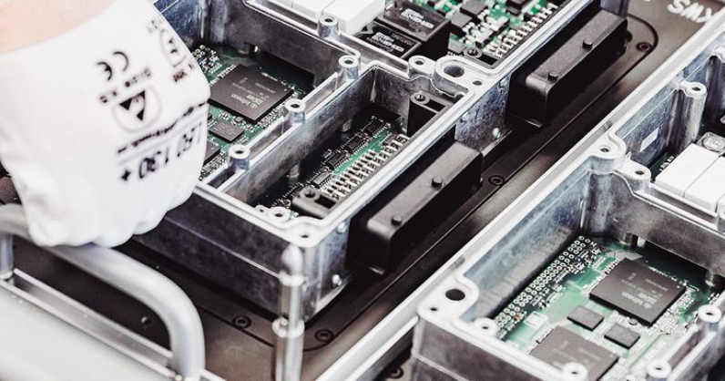 Eine behandschuhte Hand montiert oder prüft elektronische Leiterplatten in Metallgehäusen.