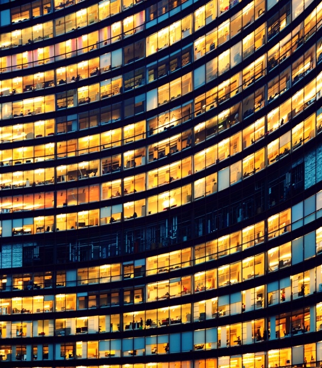 Gebogenes Bürogebäude aus Glas mit vielen beleuchteten Fenstern, die nachts leuchten.